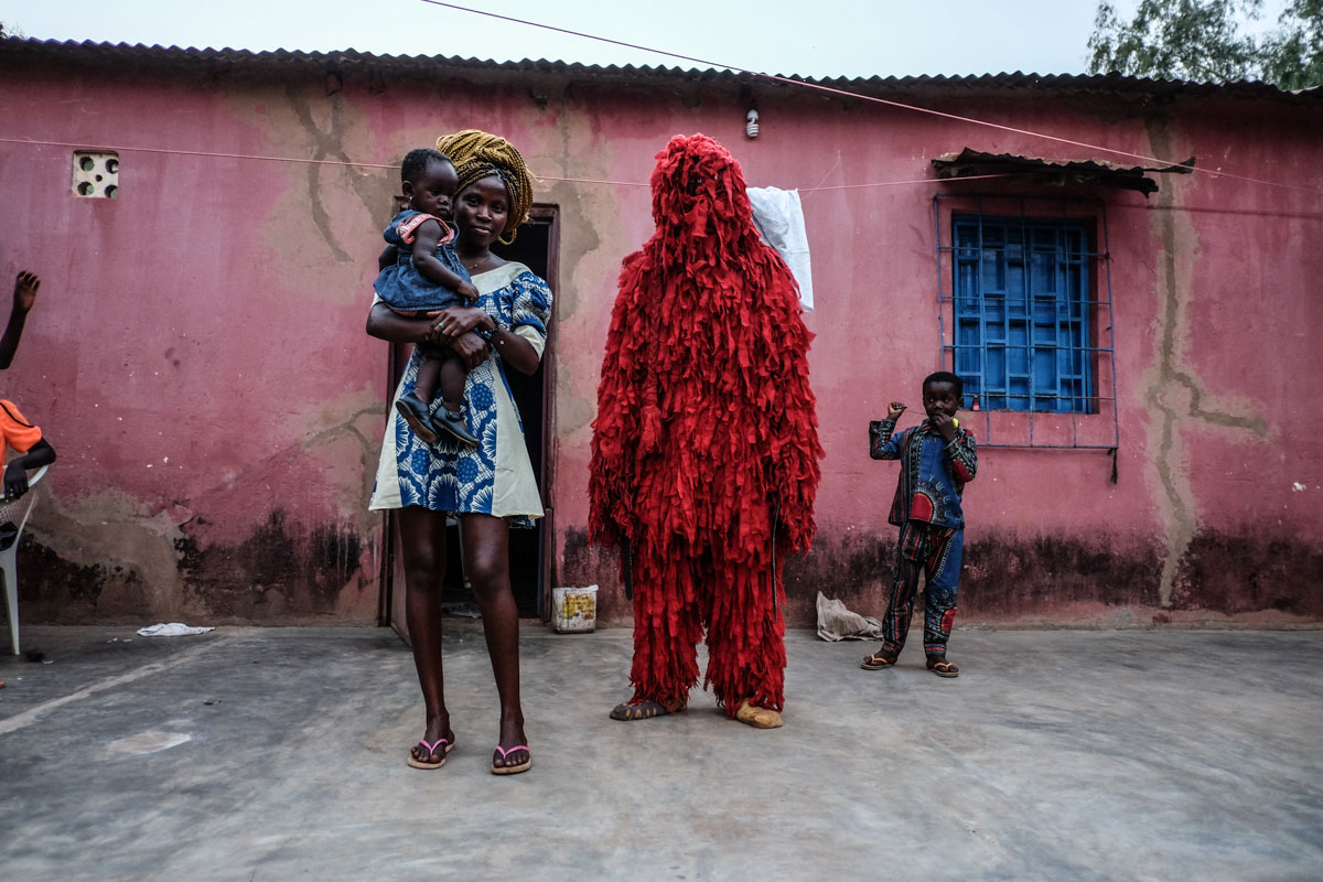 A man dressed as Kankouran, the traditional Mandinka creature that chases away evil spirits after circumcision ceremonies in Mandinka tradition, is pictured with his family in Bissau. [Ricci Shryock/Al Jazeera]